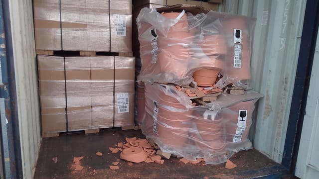 The shipment of terracotta pots on the right has collapsed, resulting in extensive breakage and debris scattered across the container floor.