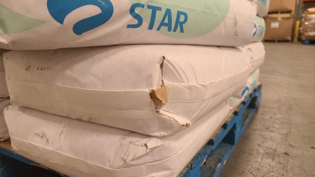 One of the stacked paper bags has a torn corner, exposing the inner packaging layer.