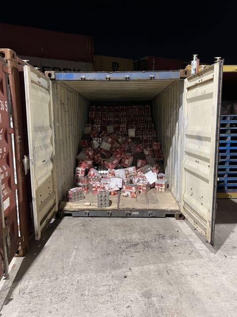 The stacked cases of canned goods inside the shipping container have collapsed and shifted forward, creating a large pile of disorganized and tumbled product.