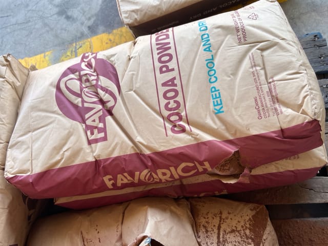 A paper sack of cocoa powder is torn open, exposing and spilling the product.