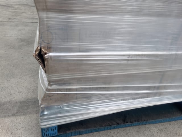 A cardboard carton on the pallet has a punctured and torn corner.